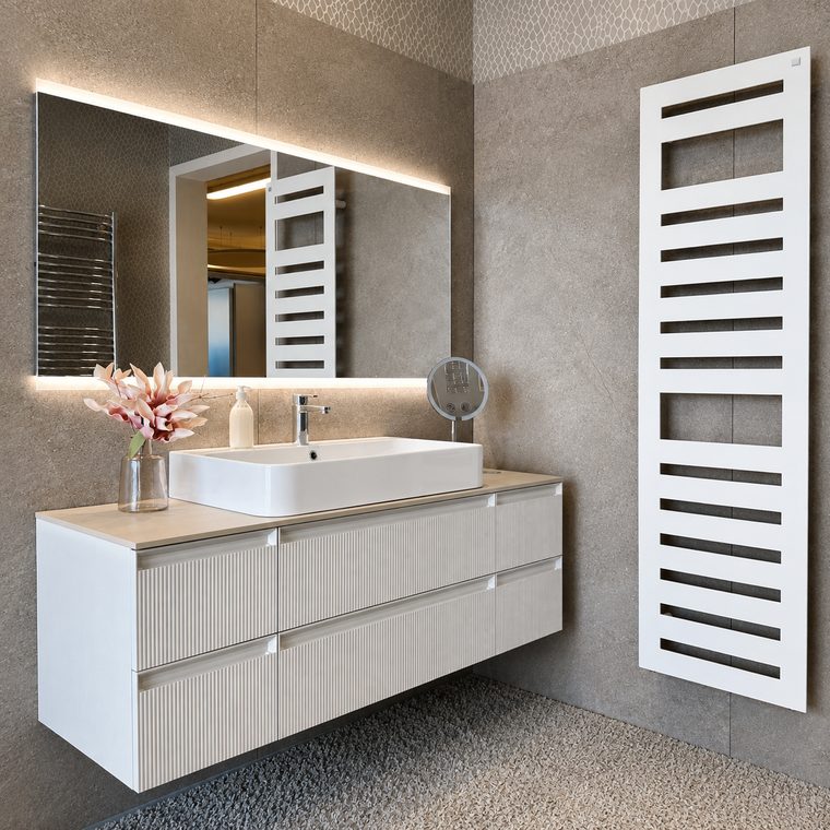Waschtisch mit geriffelten Fronten vor gro&szlig;formatigen Fliesen in Steinoptik, rechts ein wei&szlig;er Design-Heizk&ouml;rper.