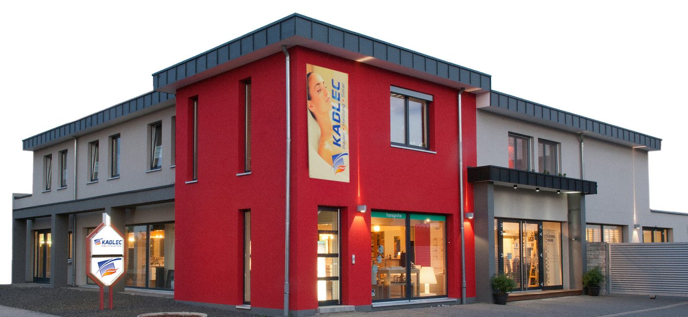 Das Betriebsgeb&auml;ude in der Nikolaus-Otto-Stra&szlig;e heute: heller Bau mit rot abgesetzter Geb&auml;udeecke, beleuchteten Ausstellungsr&auml;umen und Firmenschild an der Zufahrt.