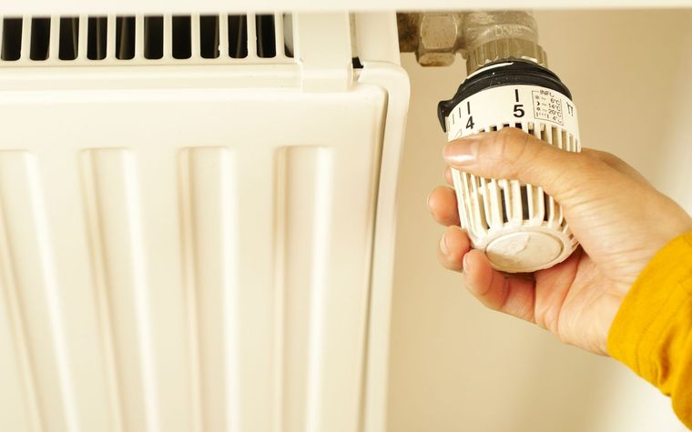 Hand stellt das Thermostatventil an einem Heizk&ouml;rper ein.