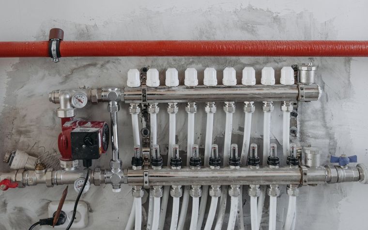 Verteiler einer Fl&auml;chenheizung mit Durchflussmessern, Pumpe und angeschlossenen Heizkreisen an einer Wand.